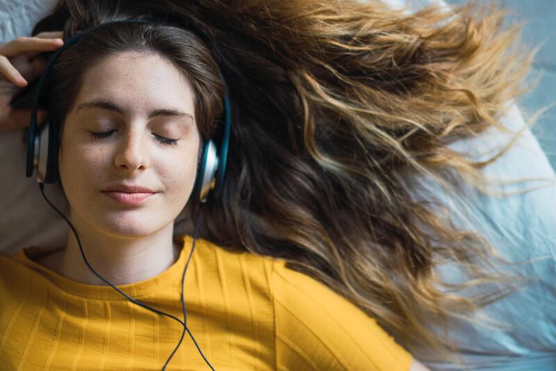 Portrait of smiling young woman lying on bed listening music with headphones. Getty Images