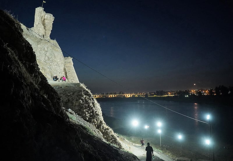 Pedestrians walk past the illuminated ruins of Qara Serai on the bank of the Tigris. AFP