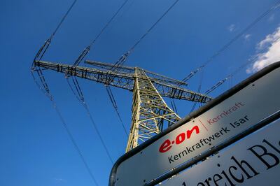 The E.ON SE logo sits on a sign as an electricity pylon carries power cables near Isar nuclear power plant in Essenbach, Germany, on Monday, July 20, 2015. In one of the most ambitious political undertakings of a modern industrial economy, Germany is shutting down all its nuclear power plants by 2022. Photographer: Krisztian Bocsi/Bloomberg