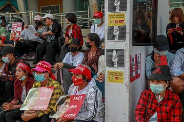 Protesters sitting next to signs to boycott Myanmar military-linked business, display pictures of deposed Myanmar leader Aung San Suu Kyi in Yangon, Myanmar on Tuesday, Feb. 23, 2021. AP