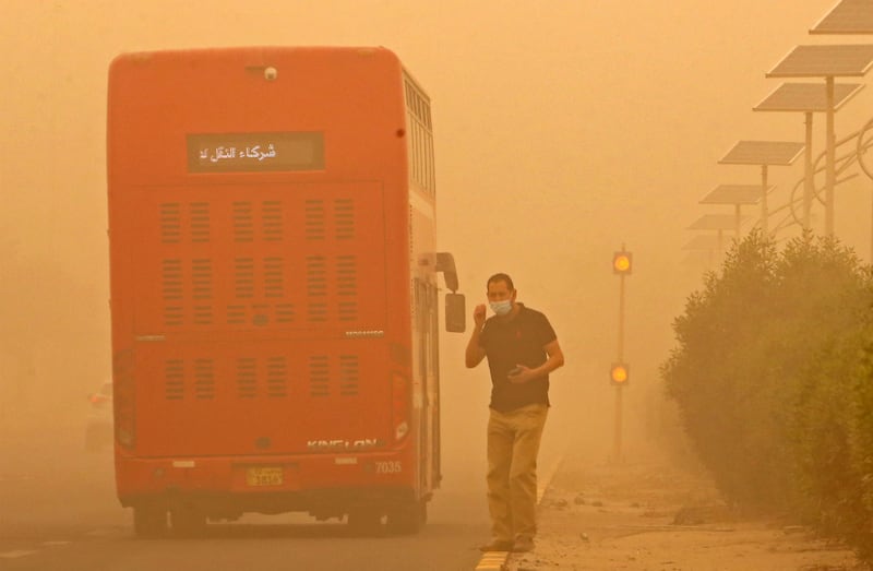 A pedestrian waits to cross a road in Kuwait City, as orange-red dust shrouds the city. AFP