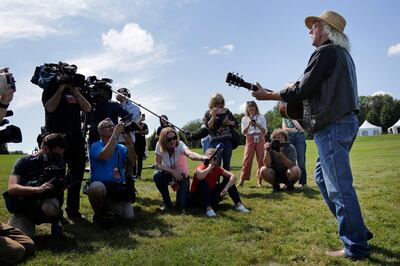 Members of the media record as Woodstock veteran Arlo Guthrie plays a song at the original site of the 1969 Woodstock Music and Arts Fair in Bethel, N.Y., Thursday, Aug. 15, 2019. Guthrie is schedule to play a set on the top of hill nearby but told reporters he wanted to play at least one song on the original 1969 site. Woodstock fans are expected to get back to the garden to mark the 50th anniversary of the generation-defining festival. Bethel Woods Center for the Arts is hosting a series of events Thursday through Sunday at the bucolic 1969 concert site, 80 miles (130 kilometers) northwest of New York City. (AP Photo/Seth Wenig)