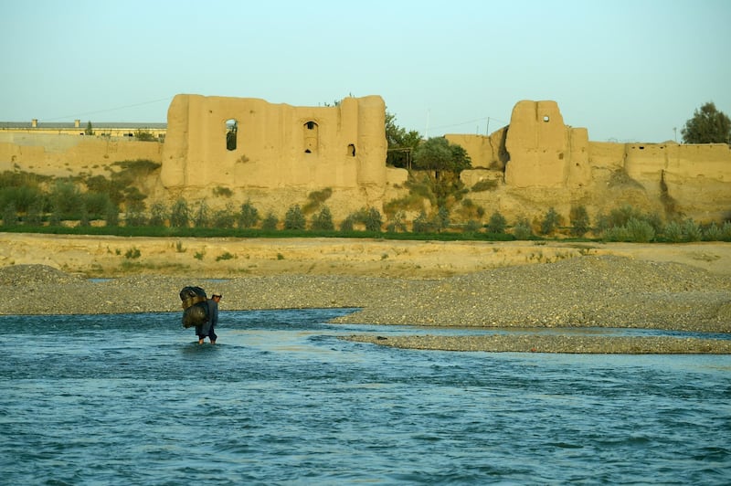 In this photograph taken on October 6, 2016 an Afghan boy carries a sack over his shoulders as he crosses a river at Lashkar Gah in Helmand province. / AFP PHOTO / WAKIL KOHSAR