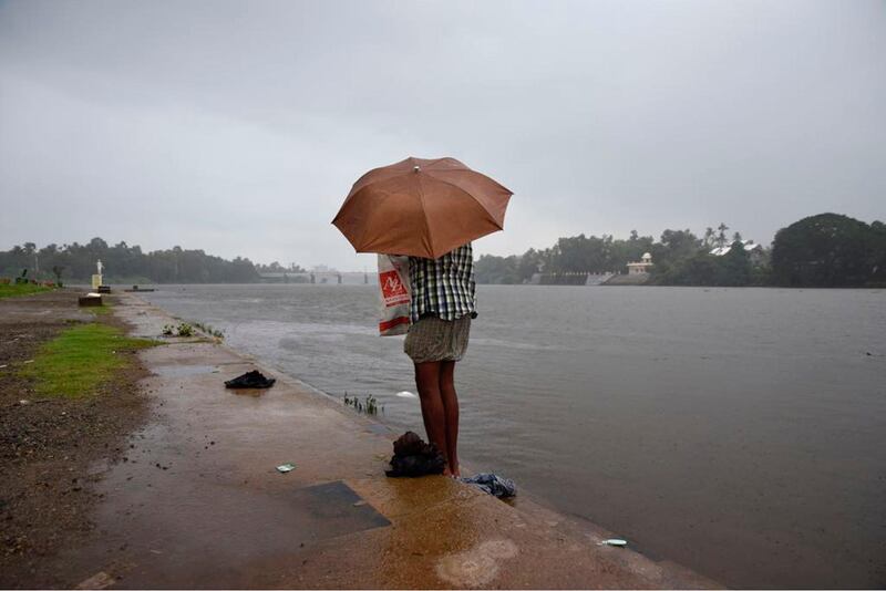 A man dresses up holding an umbrella as it started raining after he bathed in the River Periyar in Kochi, in the southern India state of Kerala, Tuesday, May 29, 2018.  The Indian Meteorological Department (IMD) said Tuesday that the southwest monsoon has arrived in Kerala and Tamil Nadu. (AP Photo/R.S. Iyer)