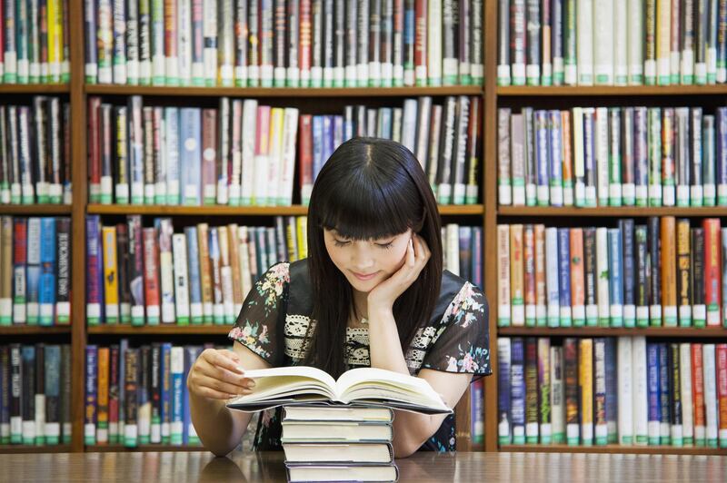 Asian woman reading book in library. Getty Images