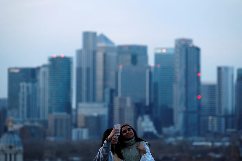 Women take a selfie overlooking Canary Wharf business district at dusk in London, Britain March 9, 2021. REUTERS/Peter Cziborra