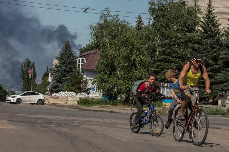 A man with children rides a bicycle along an empty street, as smoke rises after Russian shelling in Lysychansk. Reuters