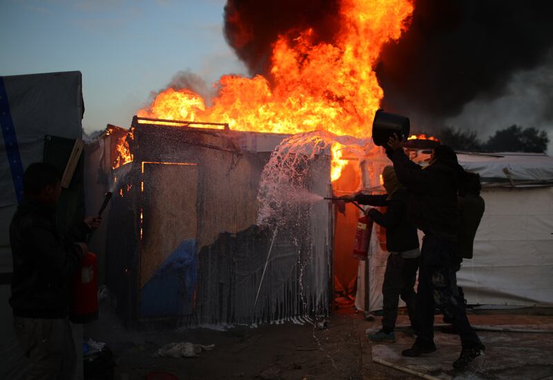 Volunteers and migrants tackle a blaze in the camp during the demolition