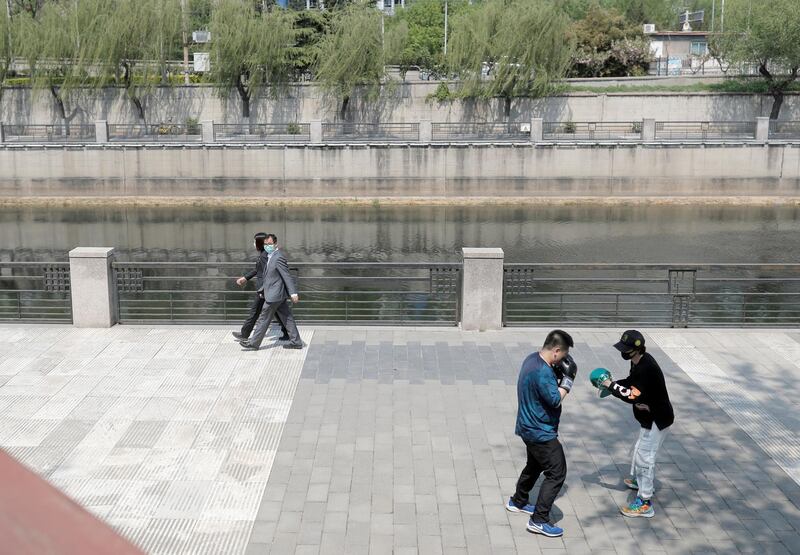 Office workers wearing protective masks walk in a park as people practice boxing during lunch hour near Beijing's Central Business District. Reuters