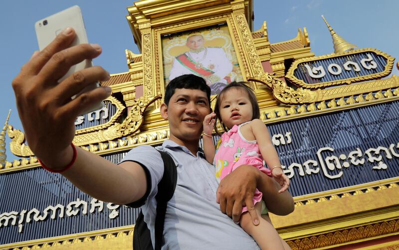 A Cambodian man takes a selfie with his daughter next to a large portrait of Cambodia's King Norodom Sihamoni in front of the Royal Palace in Phnom Penh, Cambodia. Cambodia's King Norodom Sihamoni marks his 65th birthday celebration from 13 to 15 May.  Mak Remissa / EPA