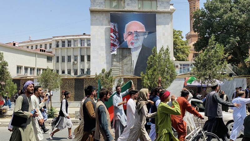 Afghans pass by the poster of Afghan President Ashraf Ghani who fled the country after Taliban took over, as they celebrate the Independence Day in Kabul. EPA