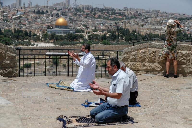 A woman grabs pictures of the Old City of Jerusalem and the closed al-Aqsa Mosque compound, as Palestinian men perform the last Friday prayer of the Muslim holy month of Ramadan at the Mount of Olives on May 22, 2020, amid the novel coronavirus pandemic crisis. (Photo by AHMAD GHARABLI / AFP)