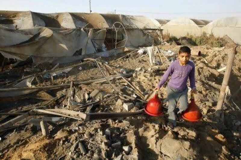 A Palestinian boy carries chicken waterers found in a coop as he walks over debris at the site of an Israeli air strike in Rafah in the Hamas-controlled southern Gaza Strip.