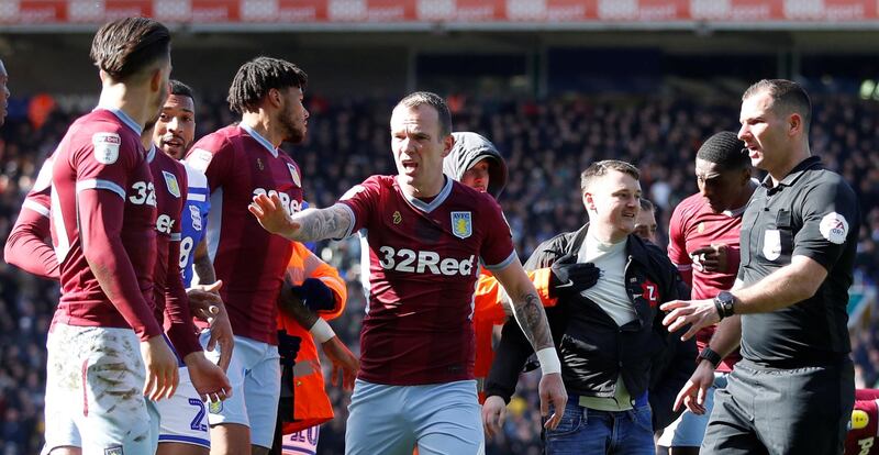 Aston Villa's Glenn Whelan gestures as a pitch invader is escorted off the pitch by stewards. Reuters