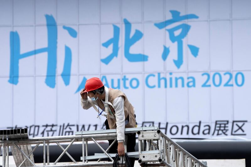 A worker labors near a sign which reads "Hi Beijing, Auto China 2020" ahead of the Auto China 2020 show to be held in Beijing. AP Photo