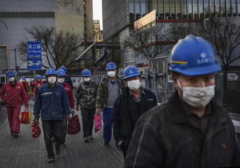 Chinese construction workers wear protective masks as they leave a site at the end of the work day in Beijing, China. Getty Images