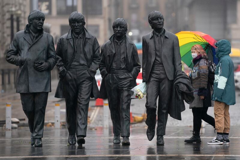 Members of the public wearing face masks stand near a statue of The Beatles in Liverpool. AP Photo