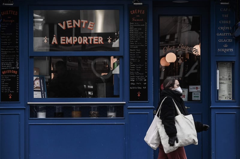 A woman carrying grocery bags walks past a restaurant selling take away food in Paris on March 16, 2020, as all non-essential public places including restaurants and cafes have been closed to prevent the spread of the Covid-19, caused by the novel coronavirus. France will progressively reduce long-distance train, bus and plane travel over the coming days in a bid to limit the spread of the coronavirus, the government announced on March 15. The country has already shuttered cafes, restaurants, schools and universities and urged people to limit their movements. / AFP / Philippe LOPEZ
