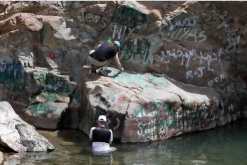 Two of the more than 100 volunteers, who turned out for yesterday's clean-up at Wadi Wurayah organised by the WWF, work on removing graffiti from the rocks. Pawan Singh / The National