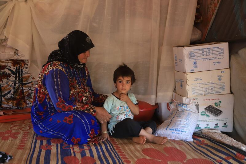 A woman with her grandchild with the rest of the food box in her tent.