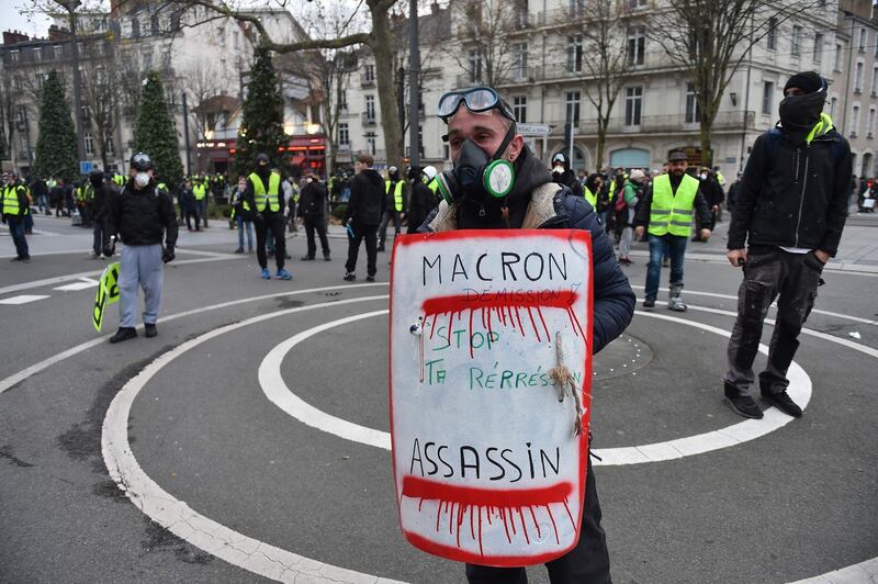 A protestor holds a placard reading "Macron resign, stop repression" during a "yellow vest" (gilets jaunes) anti-government demonstration on December 29, 2018, in Nantes, western France. Police fired tear gas at "yellow vest" demonstrators on December 29 but the turnout for round seven of the popular protests that have rocked France appeared low. The yellow vests (gilets jaunes) movement in France originally started as a protest about planned fuel hikes but has morphed into a mass protest against President's policies and top-down style of governing. / AFP / JEAN-FRANCOIS MONIER             
