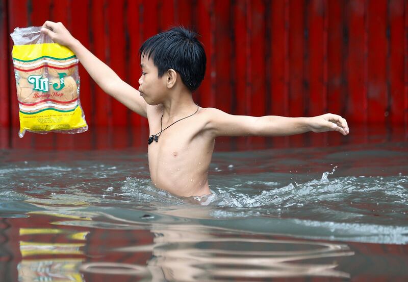 A Filipino boy carries a bag of bread while wading through floodwaters in Quezon City, east of Manila, Philippines. Rolex De La Pena / EPA