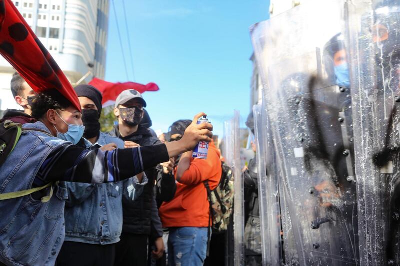 A Tunisian protester sprays liquid against the shields of police officers forming a human shield to block the access to demonstrators to the city centre. AFP