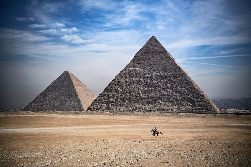 A man rides a horse in front of the pyramids of Khufu (Cheops) (L), Khafre (Chephren), at the Giza pyramids necropolis on the southwestern outskirts of the Egyptian capital Cairo, on January 26, 2021. (Photo by Anne-Christine POUJOULAT / AFP)