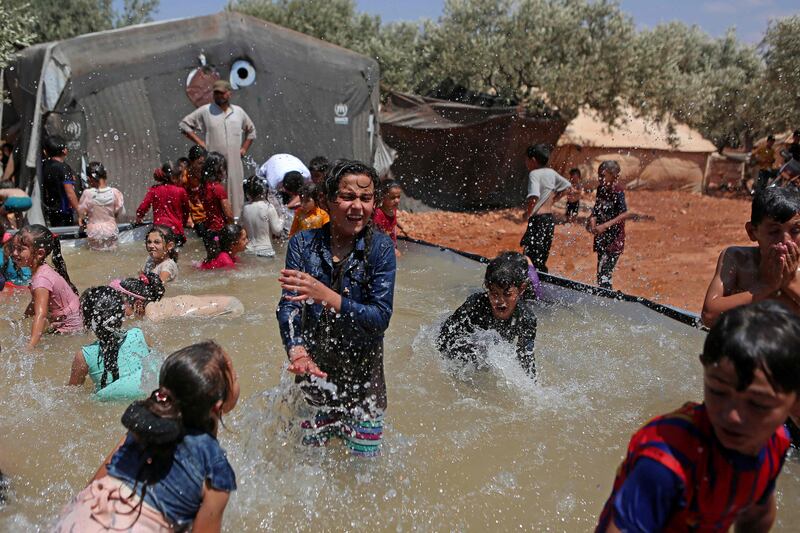 Syrian children play in a portable swimming pool set up by volunteers, at a camp for the displaced in the rebel-held town of Kafr Yahmul in Idlib. 