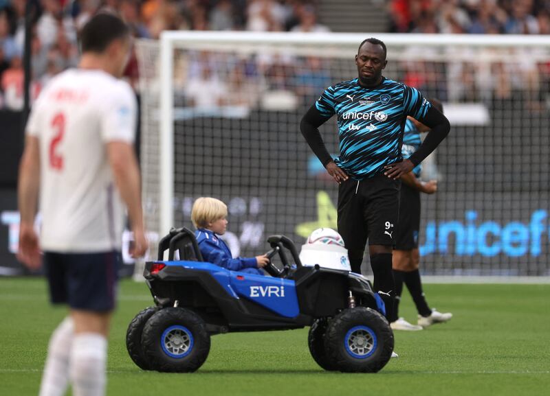 A young boy in a toy car delivers the ball onto the pitch as World XI's Usain Bolt looks on before the match. Reuters