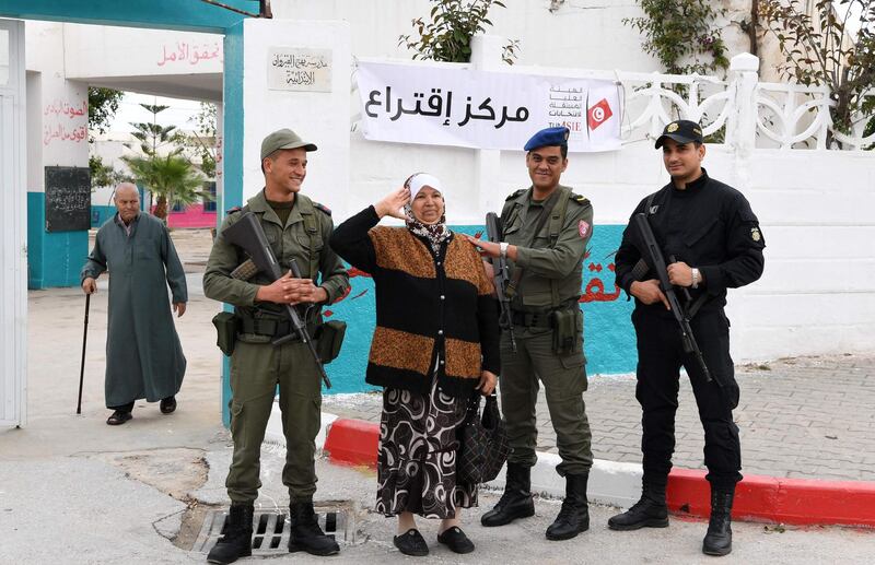 A Tunisian woman holds up her right hand in a gesture of salute as she stands between army soldiers and next to a policeman (R) standing on guard outside a polling station in Ben Arous near the capital Tunis on May 6, 2018, during the first free municipal elections since the 2011 revolution.
Tunisians head to the polls on May 6 in what is seen as another milestone on the road to democracy in the birthplace of the Arab Spring, despite muted interest in the poll as struggles with corruption and poverty continue.
Though parliamentary and presidential votes have taken place since the fall of dictator Zine El Abidine Ben Ali, municipal polls have been delayed four times due to logistic, administrative and political deadlocks. / AFP PHOTO / FETHI BELAID