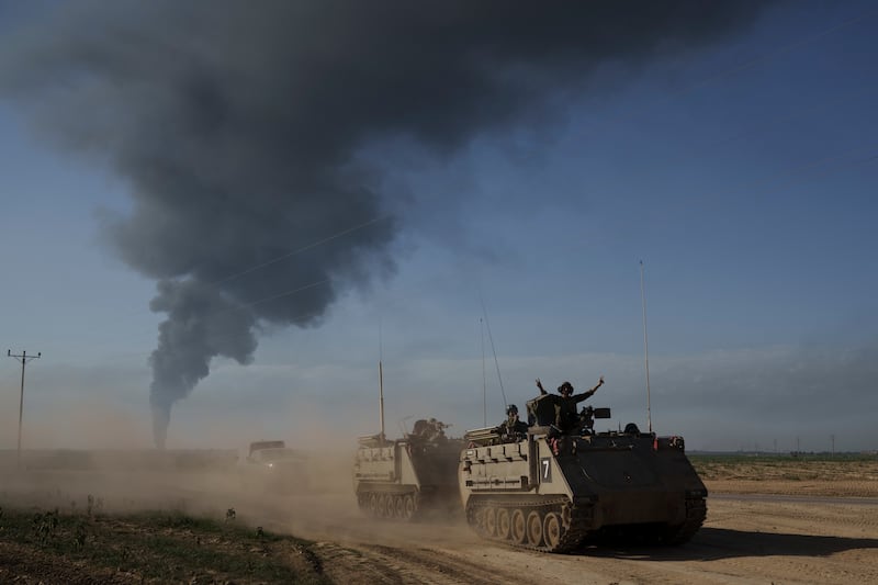 Israeli soldiers travelling in armoured vehicles near the Israeli-Gaza border as smoke rises in the background. AP