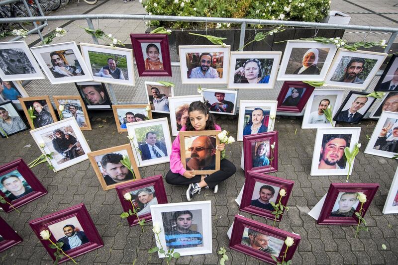 Syrian campaigner Wafa Mustafa sits between pictures of victims of the Syrian regime as she holds a picture of her father, during a protest outside the trial against two Syrian alleged former intelligence officers accused for crimes against humanity, in the first trial of its kind to emerge from the Syrian conflict, on June 4, 2020 in Koblenz, western Germany. - Wafa was part of the resistance against the Syrian government and had to flee Syria once her dad was arrested. She came to Germany in 2016. (Photo by Thomas Lohnes / AFP)