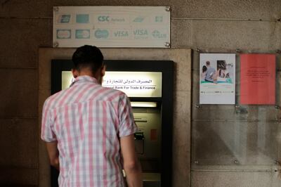 FILE - In this July 24, 2019 file photo, a man stands in front of an ATM machine outside a branch of the International Bank for Trade and Finance, in Damascus, Syria. The Syrian pound has hit a record low amid the countryâ€™s grinding war and as a financial and political crisis roils neighboring Lebanon, Syriaâ€™s economic lung. The dollar was worth 920 Syrian pounds at some exchange shops on Monday, Dec. 2, 2019, in the capital, Damascus, a sharp drop from recent days. (AP Photo/Hassan Ammar, File)