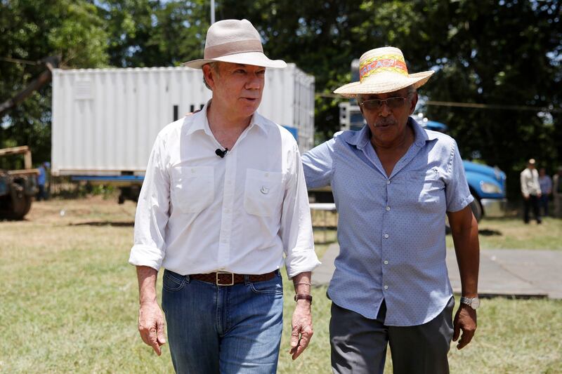 Colombia's President Juan Manuel Santos, left, walks with Joaquin Gomez, leader of the Revolutionary Armed Forces of Colombia, FARC, at a demobilization site in Fonseca, Colombia, Tuesday, Aug. 15, 2017. The weapons once carried by guerrillas had being locked up in containers guarded by U.N. observers in demobilization sites. Santos attended the ceremony to lock the final container before it was removed from the transition zone in northern Colombia. (AP Photo/Fernando Vergara)