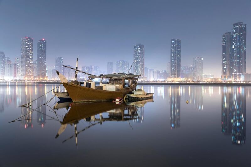 SHARJAH, UNITED ARAB EMIRATES. 30 September 2017. STANDALONE. The Sharjah skyline lights reflect in the Al Khan Lagoon while moored vessels wait out the humid night. (Photo: Antonie Robertson/The National) Journalist: None. Section: Standalone.