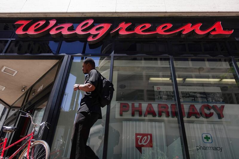 FILE - In this June 25, 2016, file photo a person walks by signage hangs outside a Walgreens pharmacy in downtown Cincinnati. The company said Monday, Nov. 4, that it will close 150 Walgreens-run clinics by the end of the year, but it will keep open more than 200 that are run in partnership with health care providers. (AP Photo/John Minchillo, File)