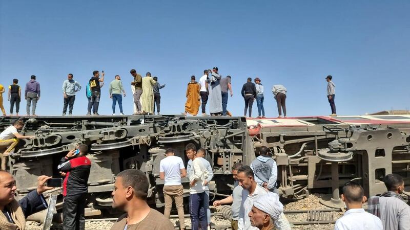 People stand atop a turned over train carriage as others inspect the scene of a train crash in Sohag province. EPA