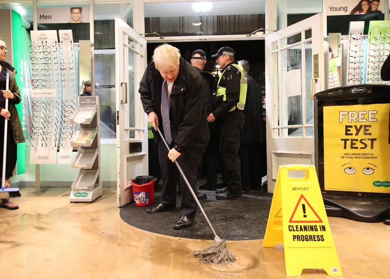 Britain's Prime Minister Boris Johnson helps with the clean up at an opticians in Matlock, northern England, on November 8, 2019 after it was effected by flooding.  Over a month's worth of rain fell on parts of England Thursday, with some people forced to evacuate their homes, and others left stranded in a Sheffield shopping centre. / AFP / POOL / Danny Lawson
