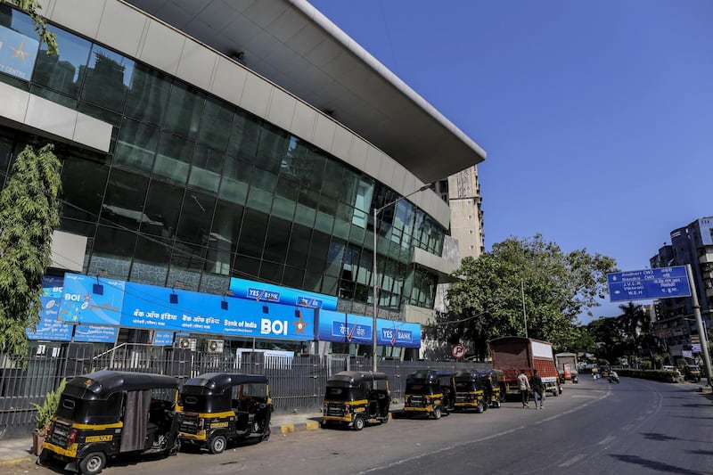 Auto-rickshaws sit parked outside branches of Bank of India and Yes Bank Ltd. on a near-empty street in Mumbai, India. Bloomberg