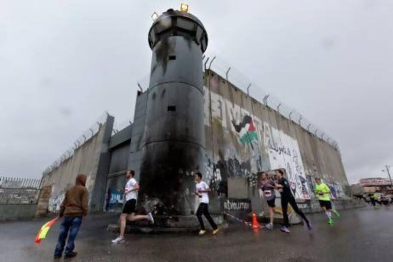 Participants in the Right to Movement Palestinian Marathon pass an Israeli guard tower and  'separation barrier,' as they run in Bethlehem.
