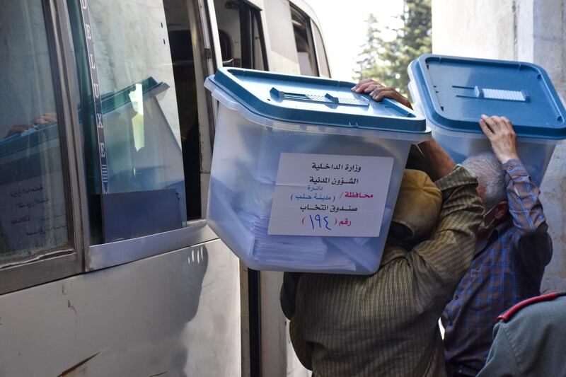 Syrian men carry ballot boxes onto a bus to hand them over to the police, who in turn will deliver them to polling stations on the eve of the parliamentary elections, in the Syrian city of Aleppo on July 18, 2020. More than 7,400 polling stations will open at 0430 GMT in government-held parts of Syria, including for the first time in former opposition strongholds. / AFP / -
