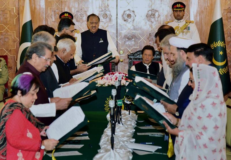 In this photo released by Press Information Department, Pakistan's President Mamnoon Hussain, center left, administrates oath of office to federal ministers while Prime Minister Imran Khan, center right, looks on during a ceremony at a presidential palace in Islamabad, Pakistan, Monday, Aug. 20, 2018. Pakistan's 21-member Cabinet was sworn in Monday, a day after Prime Minister Imran Khan pledged to cut government spending, end corruption and repatriate public funds. (Press Information Department via AP)