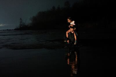 A man carries a young girl on his shoulders as he and a group of several hundred migrants wade across the Rio Grande into Eagle Pass, Texas, from Mexico. Reuters