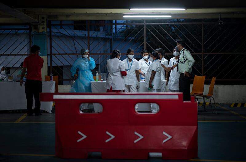 Health workers converse during a drive in facility for COVID-19 vaccination at a car parking area of a shopping mall in Kochi, Kerala state, India.  AP