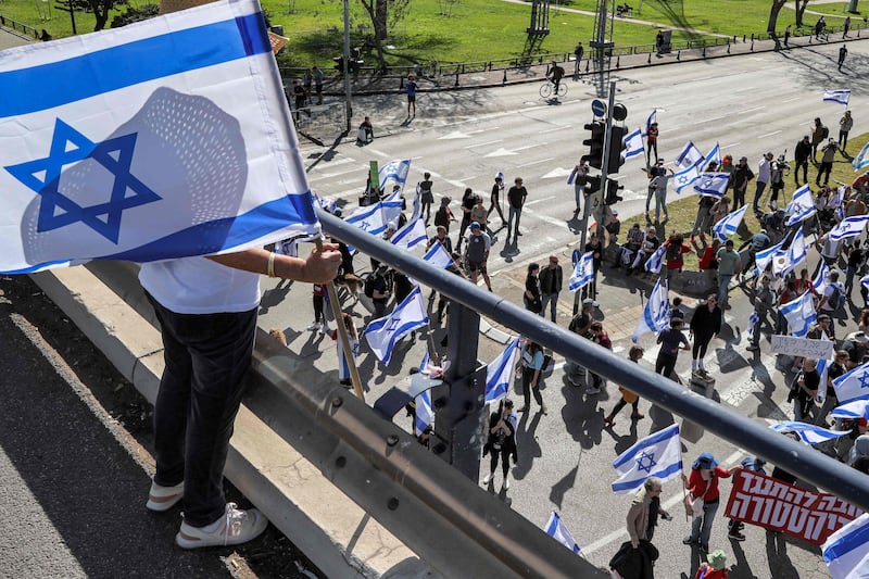 A demonstrator stands with an Israeli flag on an overpass above others march in Tel Aviv. AFP