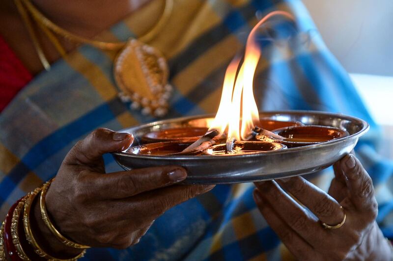 A Hindu devotee offers prayers while holding oil lamps or diyas during Diwali, the Hindu festival of lights, at a temple in Colombo on November 14, 2020. / AFP / LAKRUWAN WANNIARACHCHI
