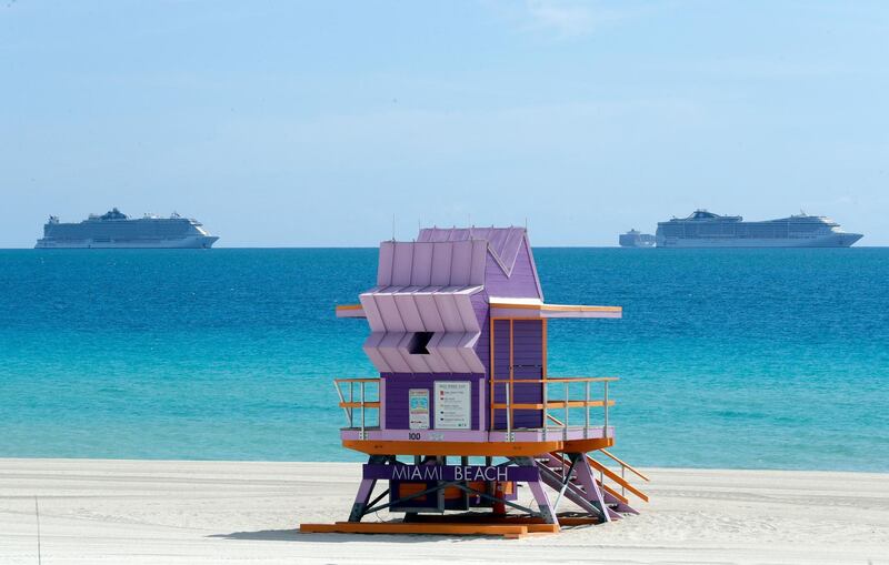 Two cruise ships are anchored offshore past a lifeguard tower in Miami Beach, Fla. AP