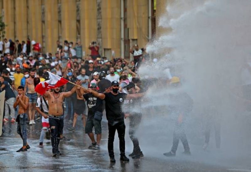Lebanese police fire water canon during clashes with demonstrators near the parliament in Beirut. Hundreds of Lebanese marched to mark a year since a cataclysmic explosion ravaged the capital.