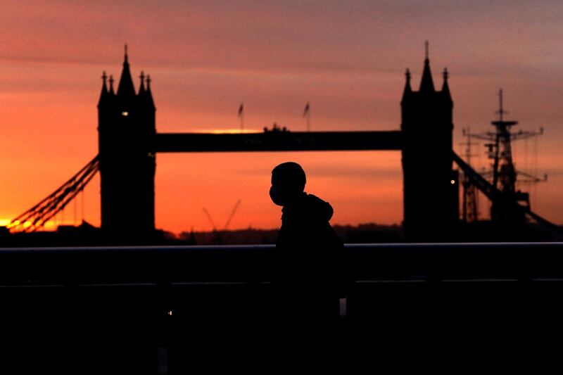 A person wearing a face mask walks across London Bridge, with Tower Bridge in the background, at sunrise in London. AP Photo